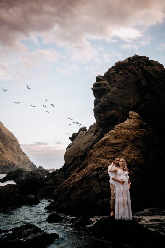 couple on the dramatic cliff in Big Sur with seabirds flying above