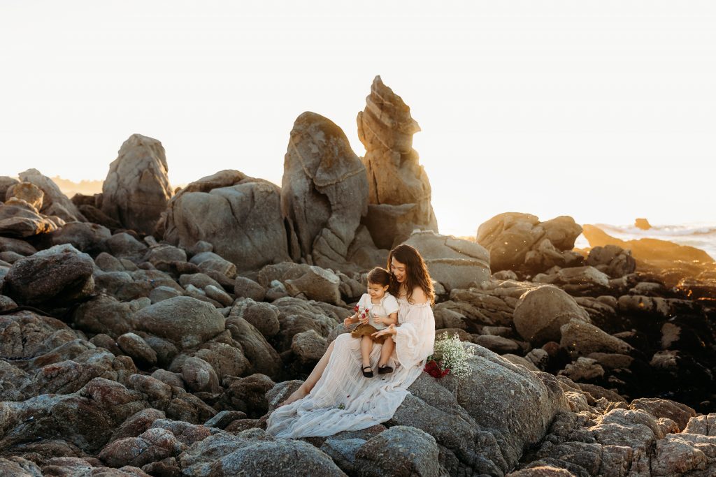 Mom and daughter playing with flowers at sunset on the rocks in carmel, California